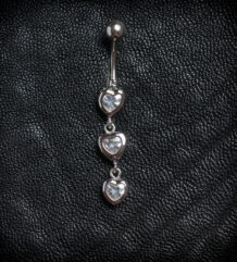 Сребриста обеца за пъп с висулка от три вертикални сърца с бели кристали на черен фон